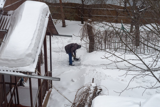 A man cleans the snow in the yard of a village house.