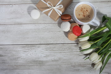 Bunch of white tulips, gifts,  macaroons and cup of coffee on white wooden table. Greeting concept. Spring, women or mothers day, cakes, cappuccino