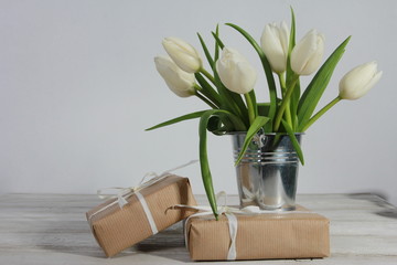Bunch of white tulips in tin bucket and gift boxes on white wooden table. Greeting concept. White ribbon, women or mothers day, spring, side view