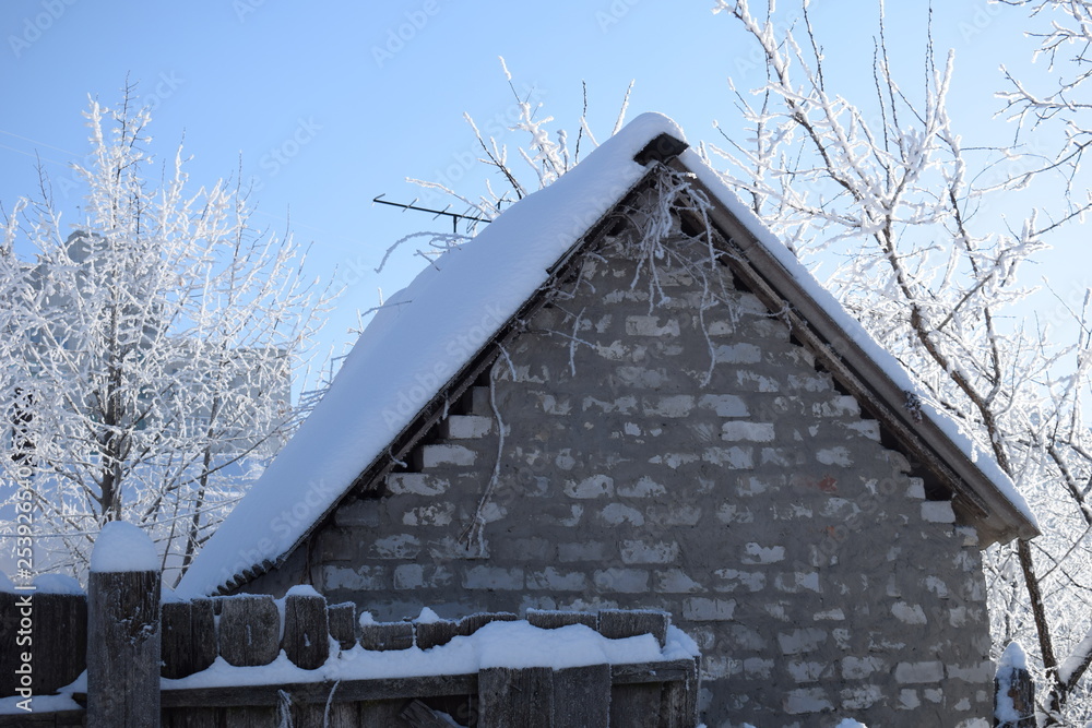 Wall mural snow covered tree branches above the snowy roof of a brick building with a blue sunny sky