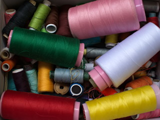 Old multi-colored coils lie in a box. A pile of coils with colored threads. Sewing supplies. Many...