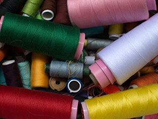 Old multi-colored coils lie in a box. A pile of coils with colored threads. Sewing supplies. Many coils of thread.