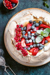 New Zealand Pavlova cake with whipped cream and mix of fresh berries on a blue textured background.
