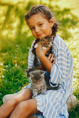 beautiful and cute girl in blue dresses with beautiful hairstyles and make-up sitting in a sunny green garden and playing with a cats
