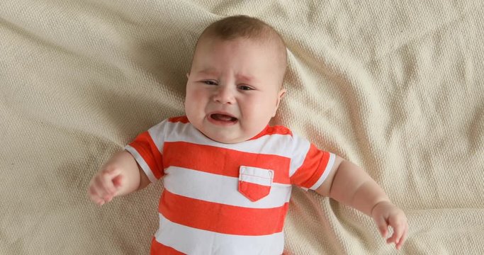 Top view portrait of crying baby, lying on the bed and call mother