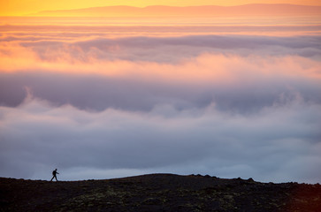 Silhouette of a man on the ridge above the sea of clouds, misty mountains at sunset in Iceland