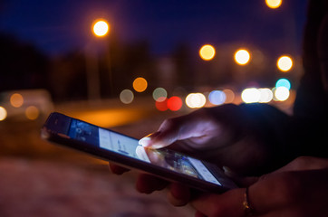 Girl pointing finger on screen smart phone on background illumination color light in night atmospheric city, hipster using in hands and text mobile phone, mock up glitter street, content lifestyle