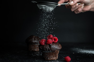 dark, romantic photo of a chocolate muffin, decorated with fresh, red raspberries. Above her a...