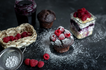 chocolate muffin with fresh raspberries sprinkled with powdered sugar in the climatic surroundings of a dark, rustic kitchen