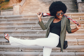 Fashionable girl in a summer city. Black lady in a green jacket. Woman in a red scarf. Famale with sunglasses