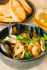 Traditional Mediterranean seafood stew in a black bowl, top view.