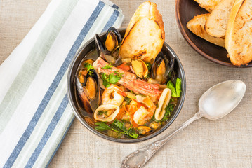 Traditional Mediterranean seafood stew in a black bowl, top view.