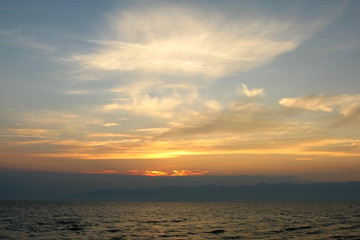 Cirrus clouds in the evening sky over water, the silhouette of the mountains on the horizon, the sun goes down. Nobody.