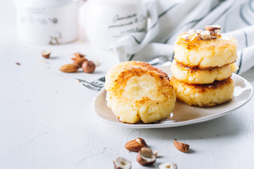 Cottage cheese pancakes with tasty honey and mixed nuts. Syrniki, curd fritters. White concrete background. Copy space