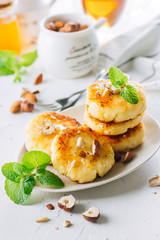 Breakfast Food Delicious Concept. Cottage cheese pancakes, syrniki, curd fritters with honey and huts on white concrete table background. Close-up