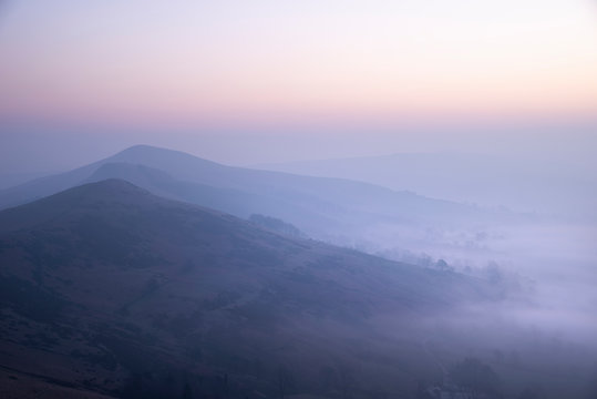Stunning Winter sunrise landscape image of The Great Ridge in the Peak District in England with mist hanging around the peaks