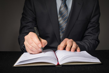Businessman writing in a diary with a pen close up.