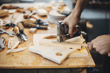 A man carves a tree. The carpenter works with stapler in a studio. An engineer provides a tree shape