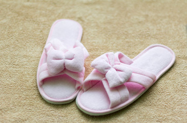 pink soft Slippers with a bow stand on a beige rug