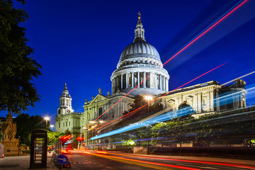 Fototapeta na wymiar Night view of the beautiful facade of St Paul's Cathedral in the City of London, London, England, with the iconic red bus passing by. The dome of the church is one of the largest in the world