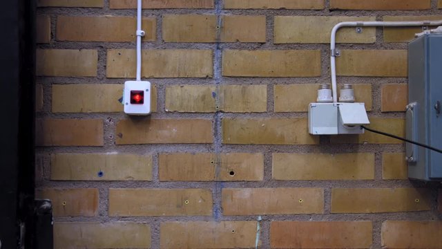 Tilt down shot of a yellow and orange brick and mortar wall, where a light switch, fusebox and electricity outlet are mounted