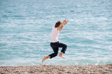 Fototapeta premium active sport healthy little boy in white shirt and blue trousers jumping on spring sea background during holiday