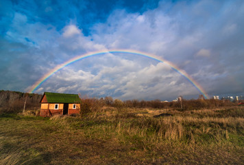 Rainbow above the field of yellow dry grass and lonely house