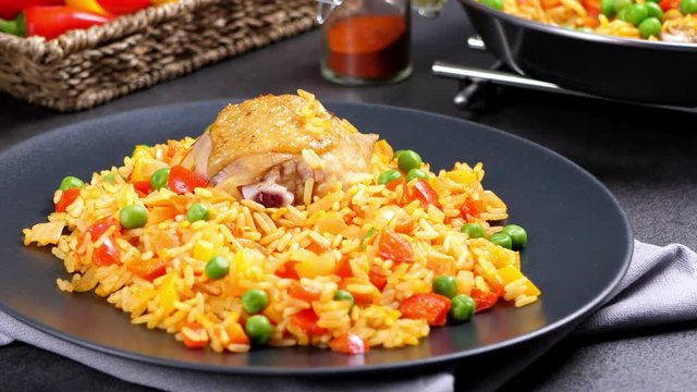 Cooking, steaming, eating, watching. Slow motion. Arroz con pollo. Baked pieces of chicken with bone, rice with paprika and peas. Black background. Served on black plate or spanish pan. 