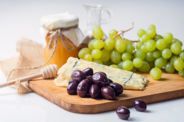 White cheese plate with olives, honey, grapes. Assortment of wine snack, appetizer or gourmet dinner. Top view