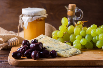 Cheese with grapes, olive, honey on wood