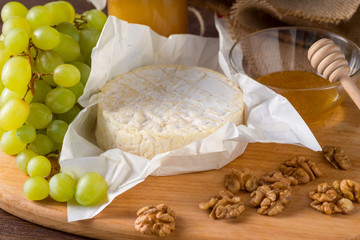 Camembert cheese on a wooden board with honey, fruits and nuts