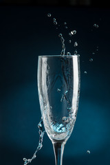 splash in a champagne glass against falling water on a dark blue background