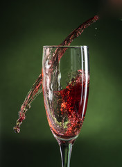 splash in wine glass from falling red wine on a dark green background