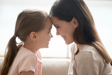 Happy kid girl and smiling mother touching foreheads, side view
