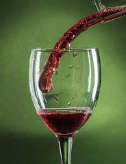 splash in wine glass from falling red wine on a dark green background