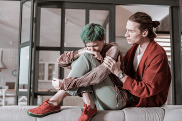 Husband wearing red jacket touching shoulder of his crying wife