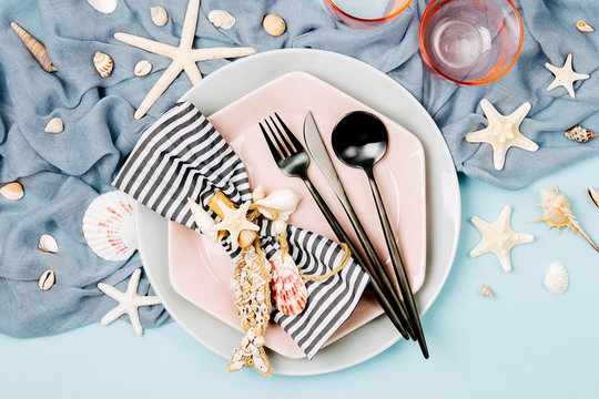 Tableware and sea decorations for serving a festive table. Plates, wine glasses and cutlery on blue background. Summer concept. Flat lay, top view