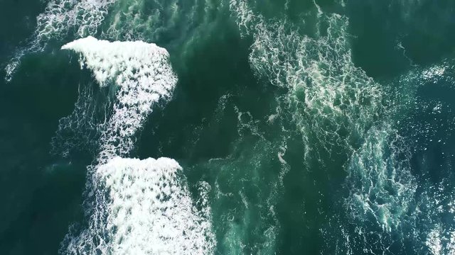 Slow Tilt Up reveal footage from crashing white on blue ocean waves to sand sculpted cliffs and puffy clouds in blue sky Sunset Cliffs, San Diego, California - 4k
