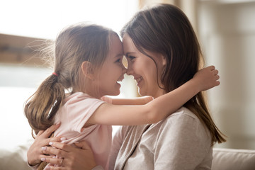 Cute kid girl embracing smiling mom touching noses having fun