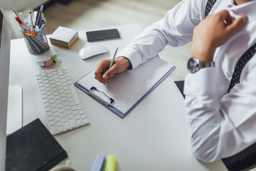 Close up, businessman holding pen at financial on wooden desk in home office. Expensive watch at his hand.