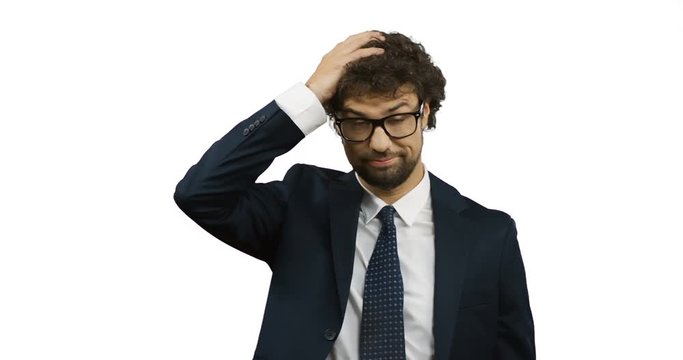 Portrait shot of the caucasian dissapointed upset man in the glasses. suit and tie touching his head with a face like everything failed. White back wall screen.
