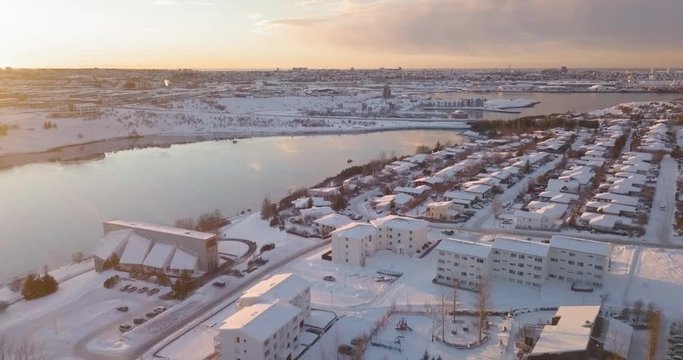 Beautiful aerial winter sunset view, modern suburb neighboorhood Reykjavik Iceland. Cold snowy evening, residential cityscape. 4k suburbian drone footage.