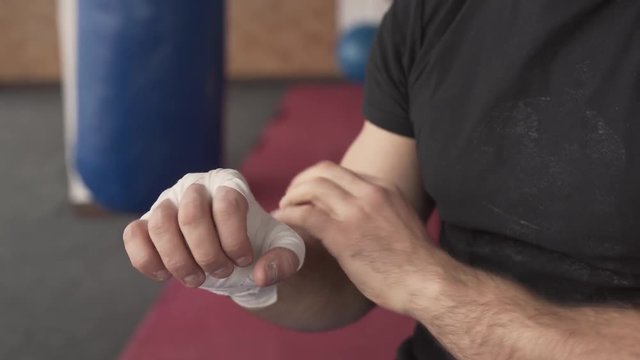 Close-up of a young athletic man wrapping his hand with white box bandage. Fitness concept. Martial arts.