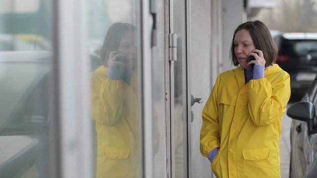 Woman in yellow raincoat talking on mobile phone in disbelief out on the street on a rainy day