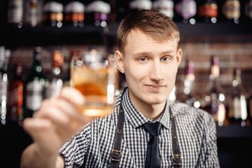 Barman holds out glass of whiskey with ice to male visitor. Concept rest in bar