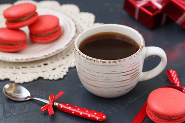 A cup of coffee on a dark background with macaroons of coral color