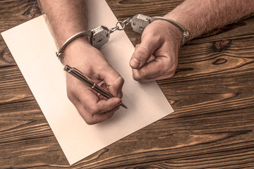 Man's hands in handcuffs, blank sheet of paper on the background of a wooden table. detention, arrest, confession.