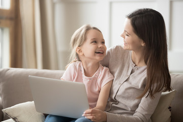 Happy mom and kid daughter laughing having fun with laptop