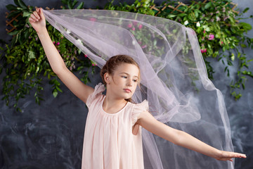 Lovely little girl playing with light fabric against the flowers background. Portrait of the nice little girl. Dancing little girl. © fadzeyeva