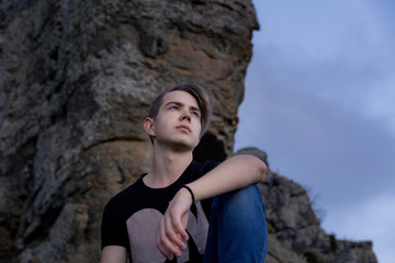 Young attractive man located with  on the top of mountains looks into the distance at sunset